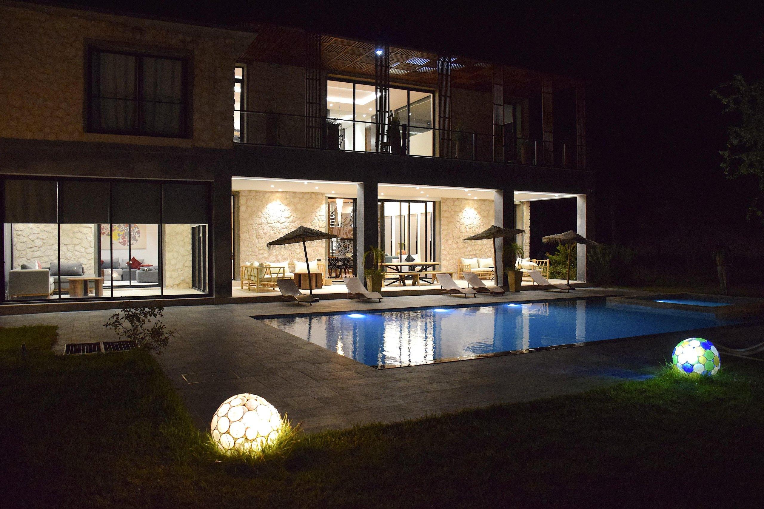 La villa éclairée de nuit, la piscine chauffée au premier plan.