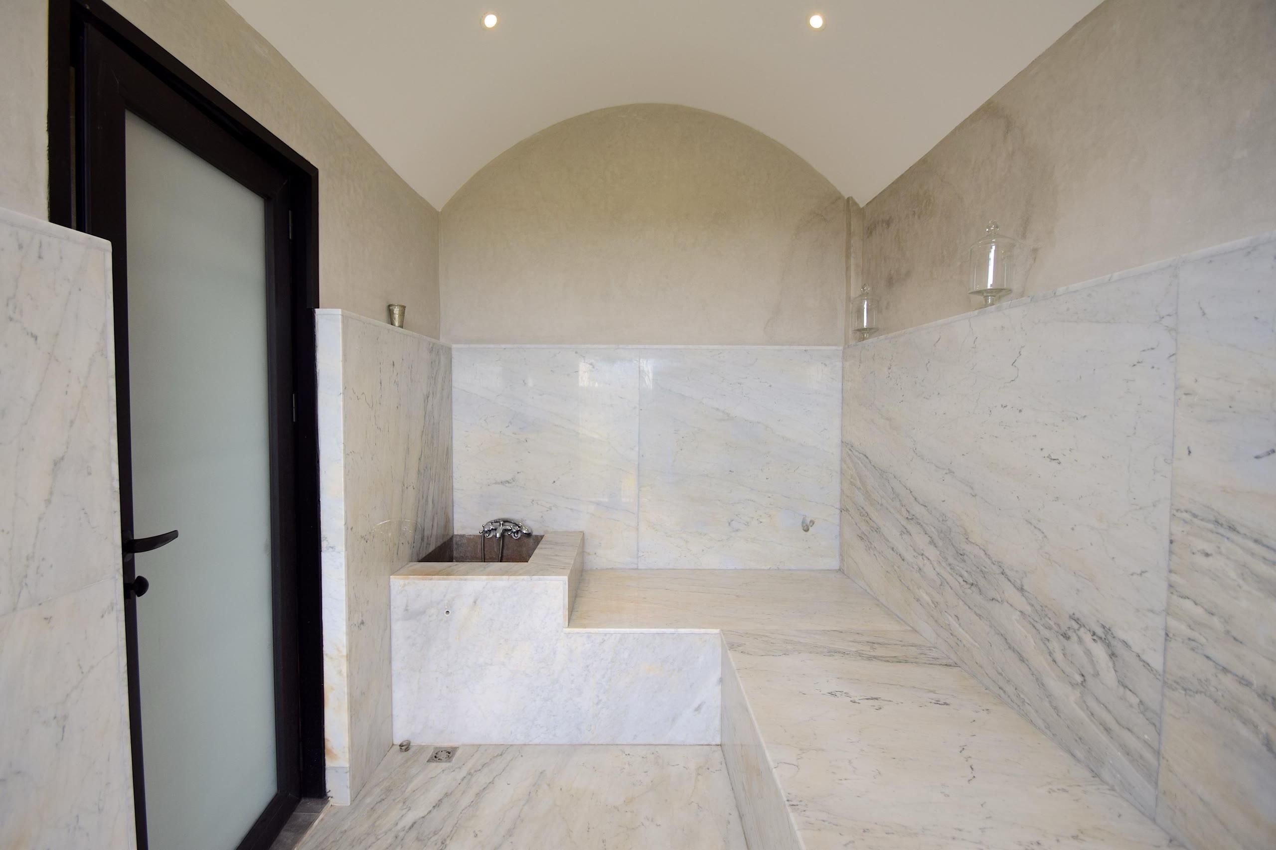 Le hammam : voûte de tadelakt, murs et banquettes de marbre blanc, vasque encastrée et robinetterie ancienne.
