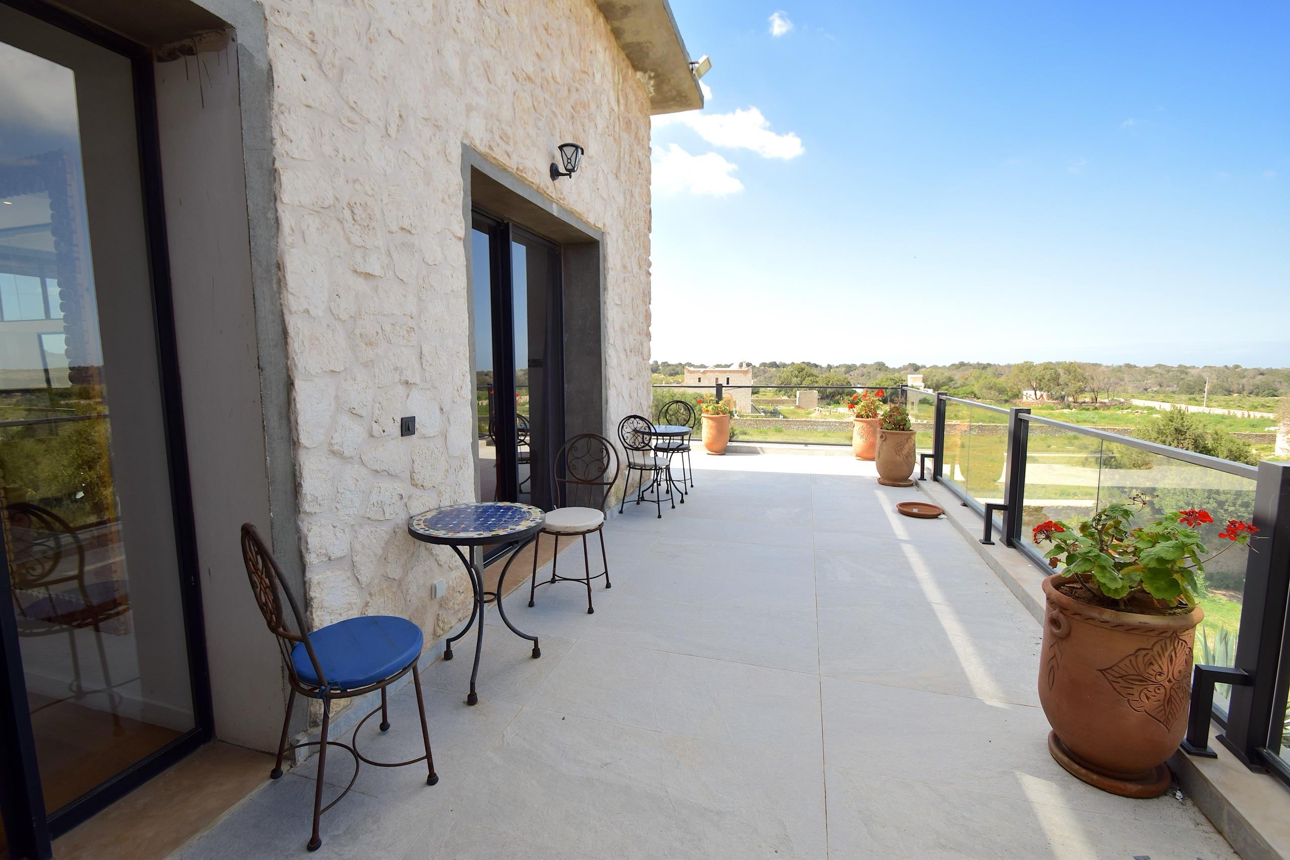 La terrasse d'étage et sa table de mosaïque, jarres de terre cuite et géraniums le long du garde-corps.